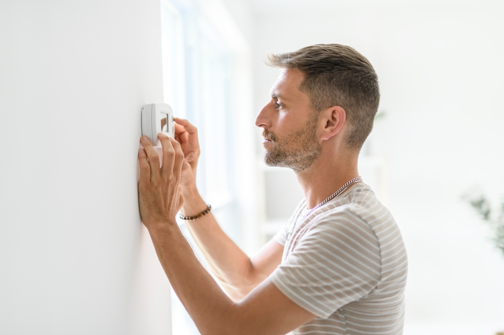 a man with a concerned look on his face as he adjusts the thermostat