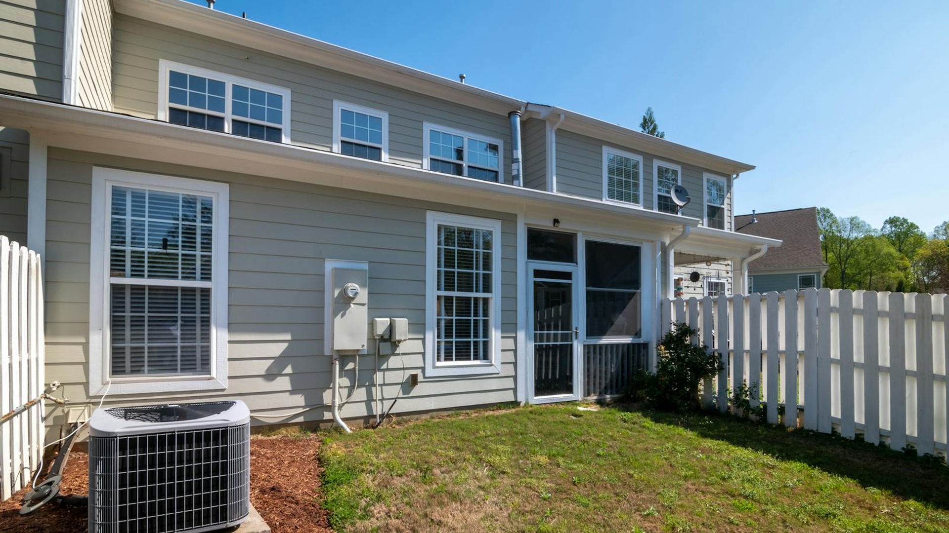 Residential central air conditioning condenser unit outside a home with vinyl siding and a white picket fence