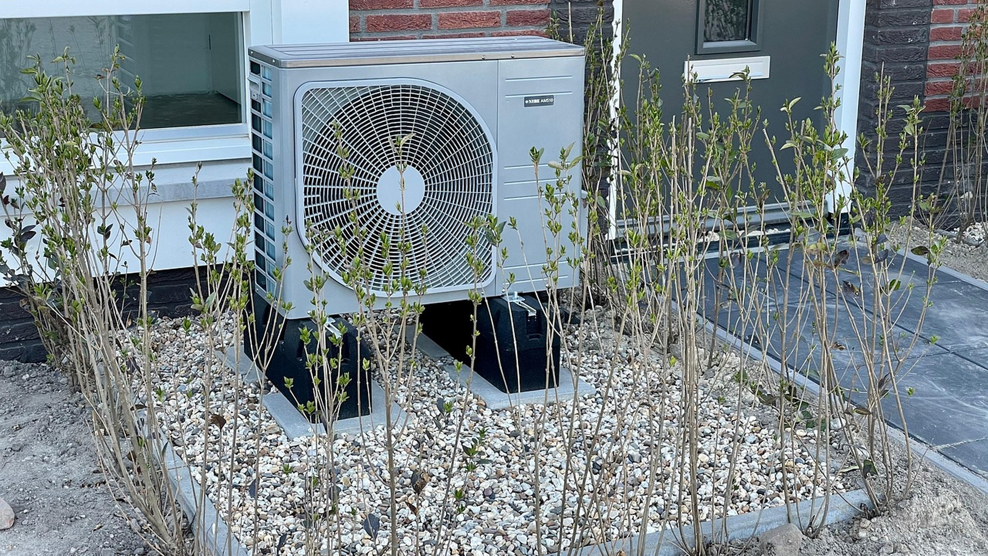 Outdoor residential air conditioner condenser unit installed beside a home with gravel landscaping