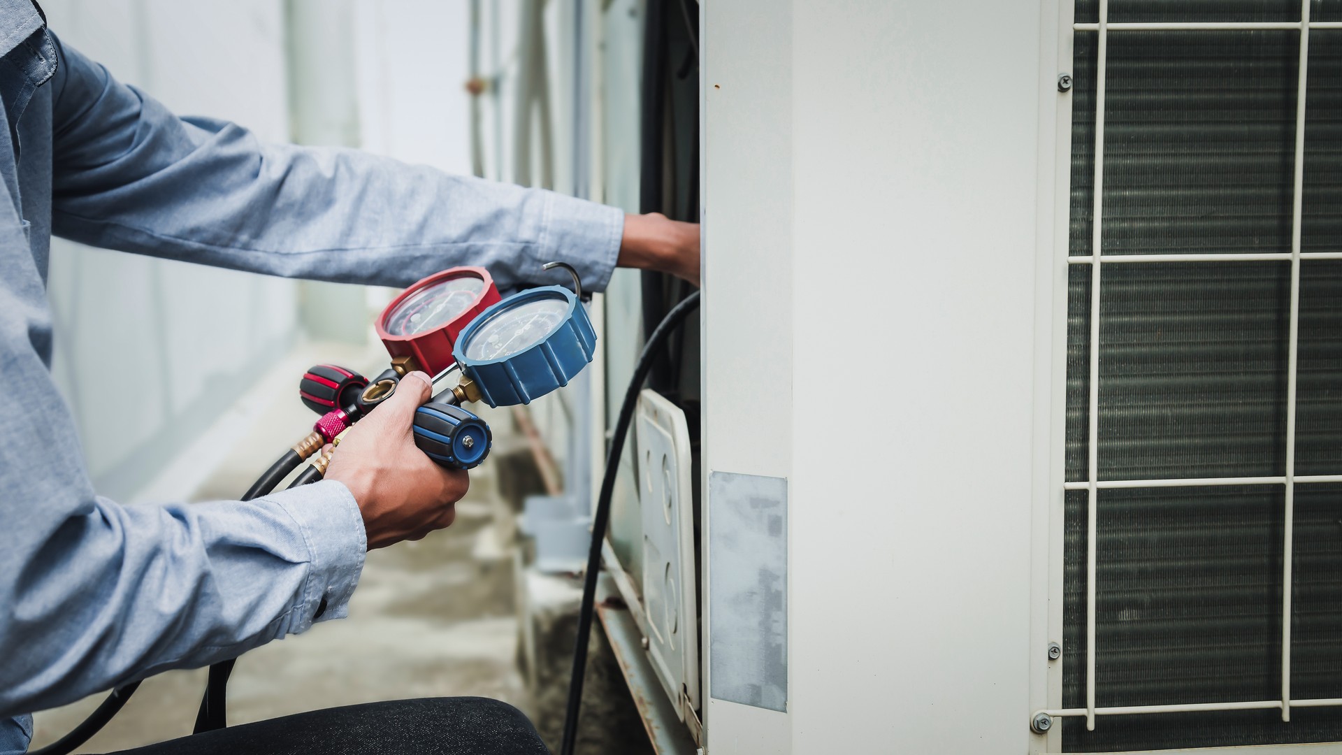 A/C technician using a manifold gauge to check refrigerant on an outdoor central air conditioning unit, the kind of service work an Honest Air comfort technician does across the Treasure Coast.