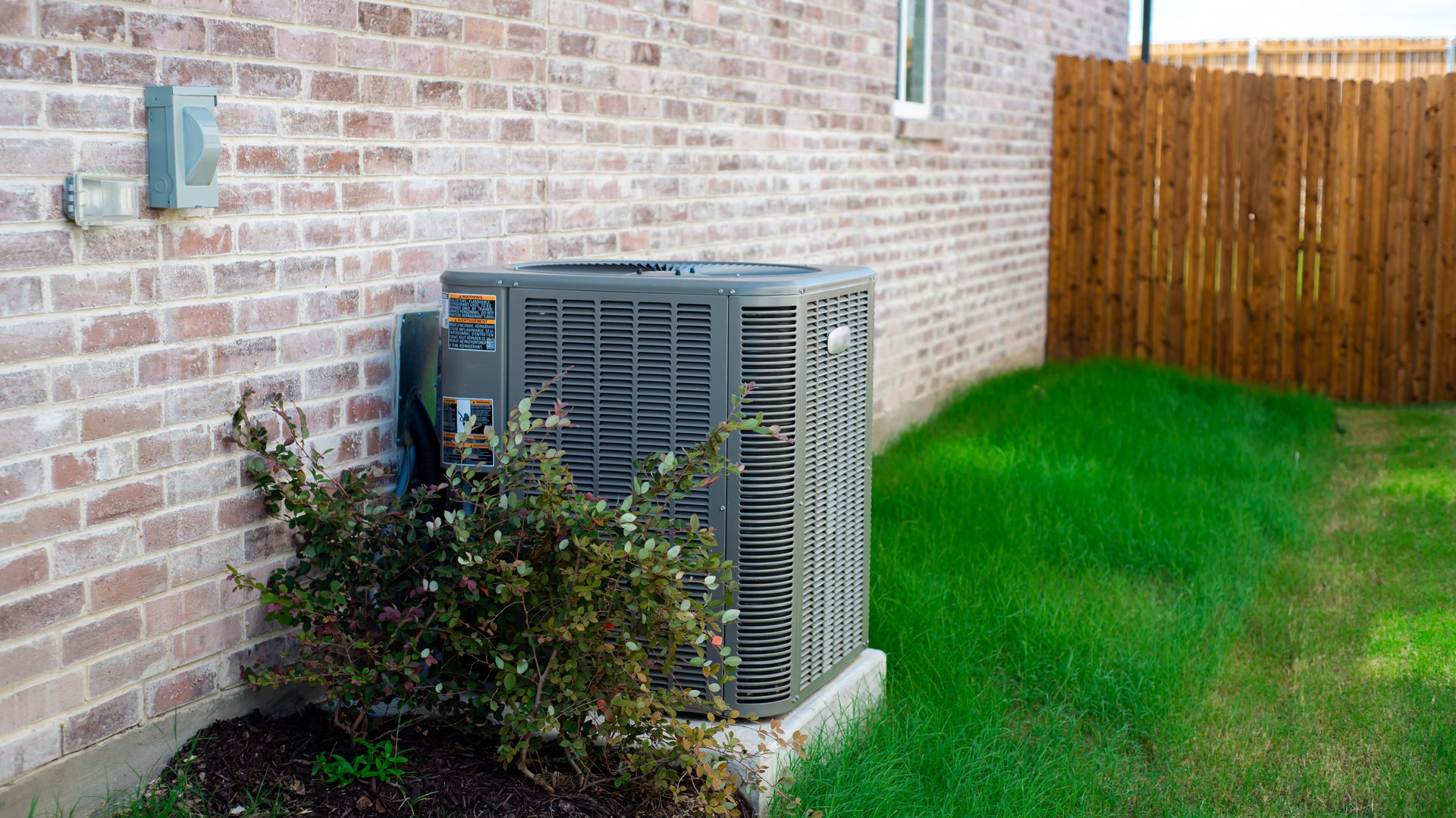 Residential outdoor central air conditioning condenser unit beside a single-family home with the wall-mounted electrical disconnect switch and utility meter visible, where an HVAC surge protector mounts before Florida storm season.