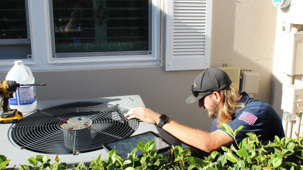 Honest Air technician examining the fan grille on top of an outdoor A/C condenser beside a Florida home